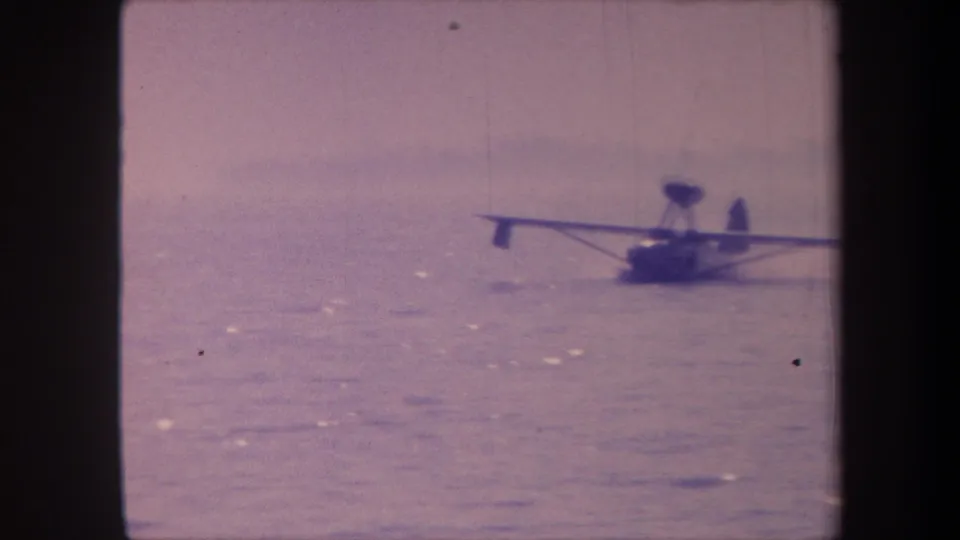 Amphibious aircraft on calm open water, c.1959, 8mm home movie with characteristic faded purple-pink color cast from film aging.