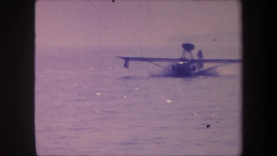 Floatplane or flying boat with visible wake on open water, c.1959, 8mm home movie with lavender-purple color shift from aging film stock.