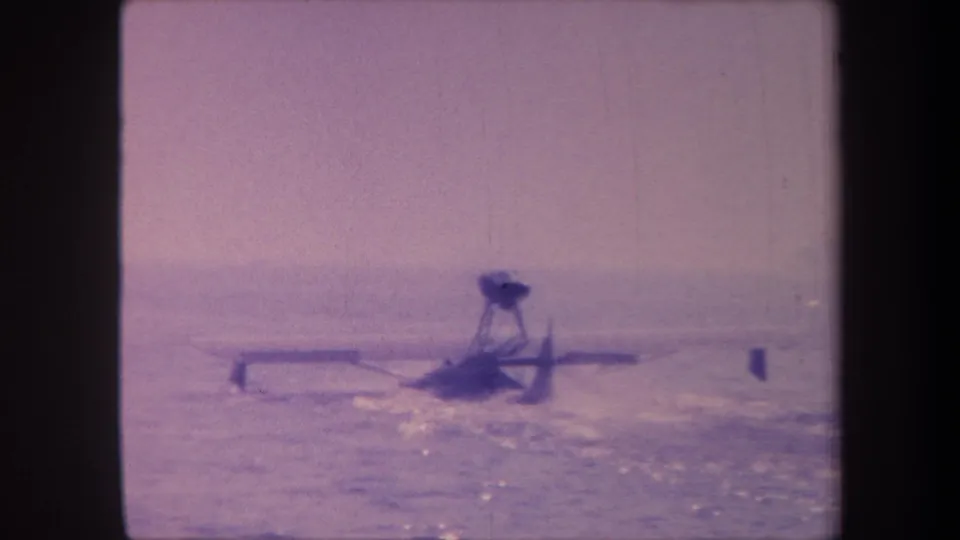 A propeller floatplane moves across choppy water in California, circa 1959; a small unidentified dark object is visible to the aircraft's right.