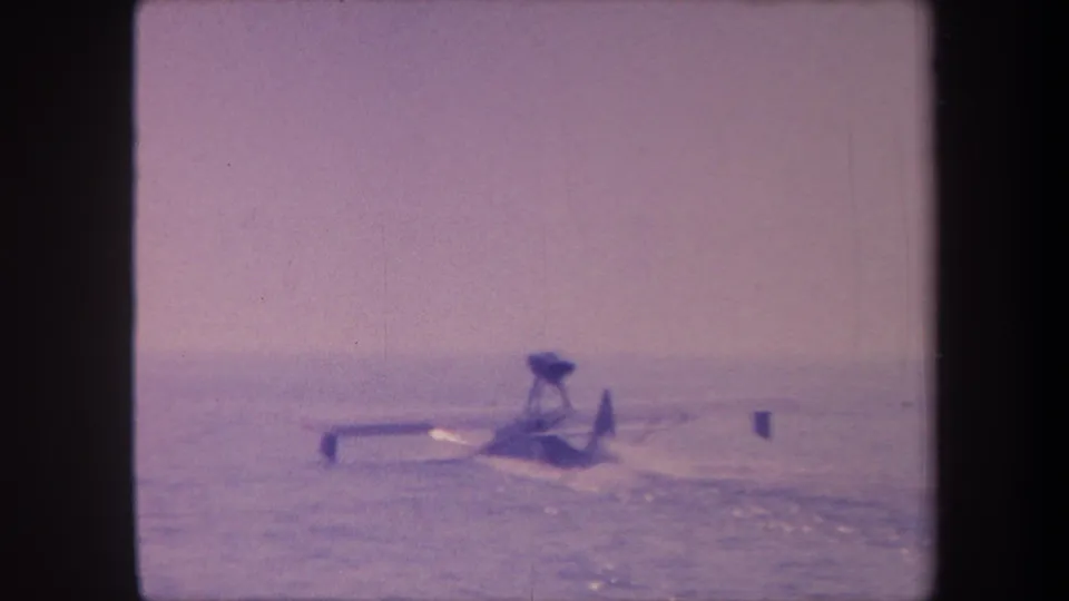 Floatplane mid-water-run in 1959 8mm footage, characteristic lavender color shift, open water surface and distant hazy horizon.