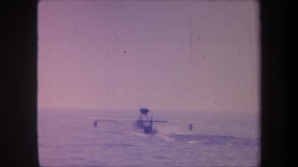 1950s 8mm home movie frame showing a hydroplane boat silhouette on open water, attributed to Yucaipa California, with heavy purple dye cast from aged film.