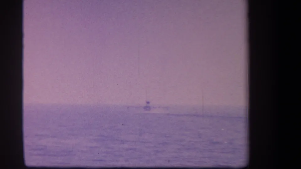 1959 8mm frame with a distant plane low on the horizon over water, seen through faded purple film color.