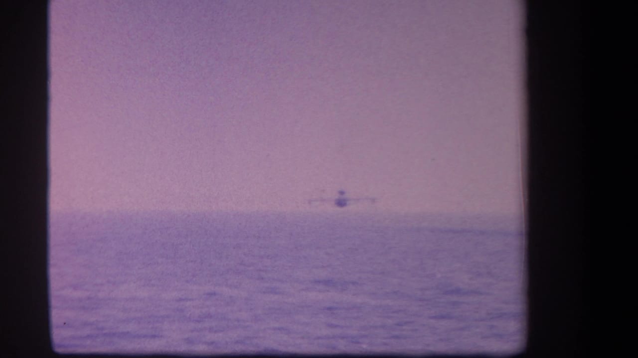 1959 8mm home-movie frame showing a small seaplane far across a calm lake in the supplied Yucaipa, California context.