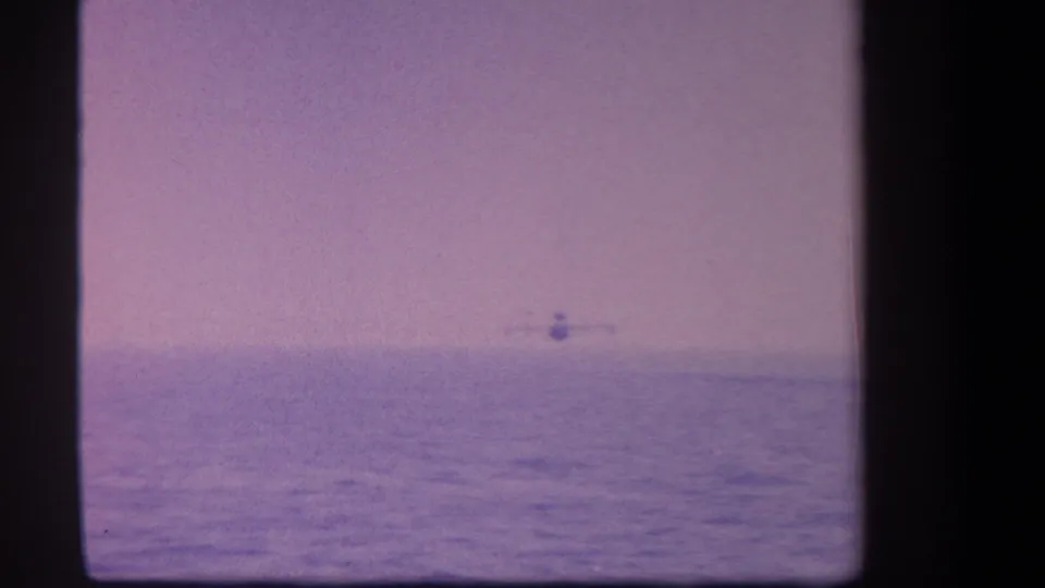 1959 8mm home-movie frame showing a small seaplane far across a calm lake in the supplied Yucaipa, California context.