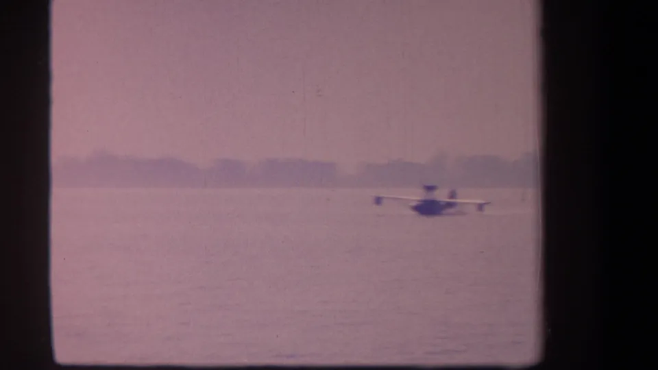 The seaplane continues across the lake in the supplied 1959 Yucaipa, California home-movie footage, framed by haze and visible film borders.