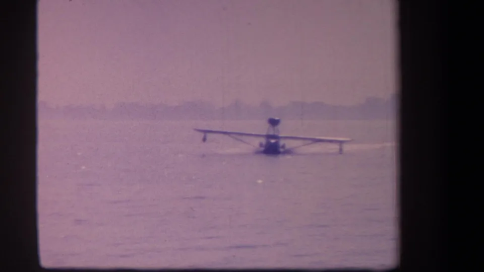 Final frame shows the small floatplane still on the water, with faded color, soft focus, and a distant tree-lined horizon.