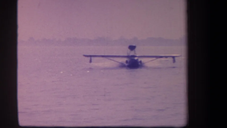 Small float plane appears centered on calm water in a faded 1959 California home-movie frame.