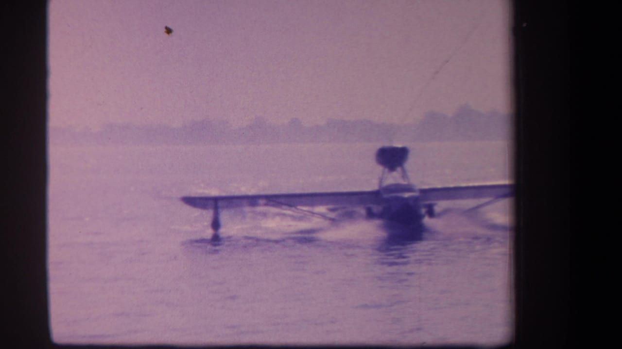 Amphibian aircraft facing the camera while taxiing on calm water.