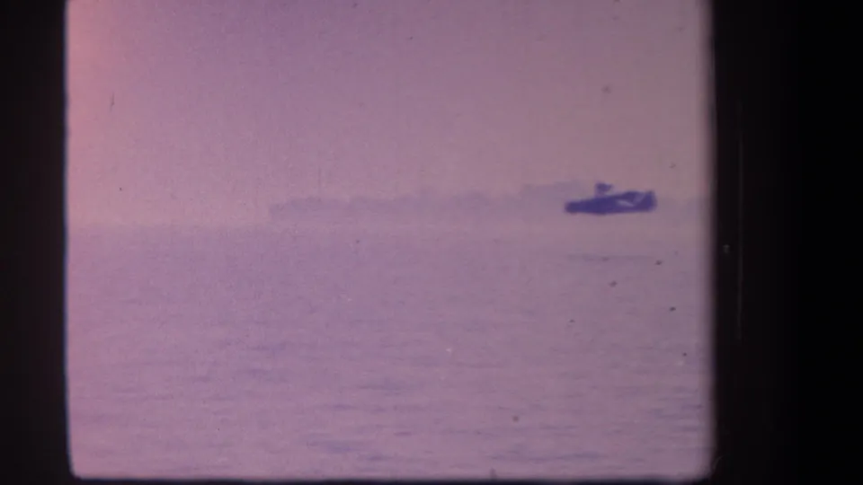 1959 8mm frame from Volmer Yucaipa area showing a distant hydroplane-like craft on calm water beneath a hazy pink-purple sky.