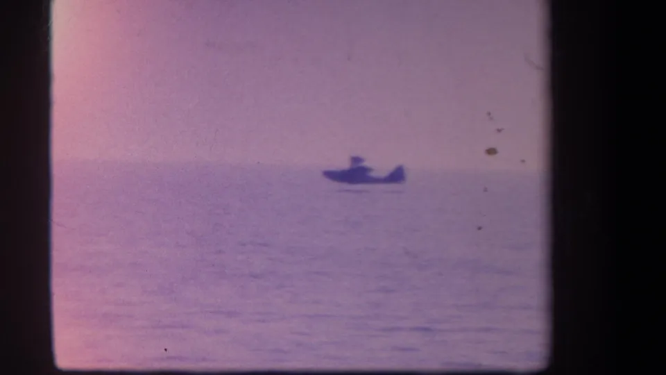 A small hydroplane-like craft appears low on calm water in a grainy, color-faded 1959 home-movie frame.