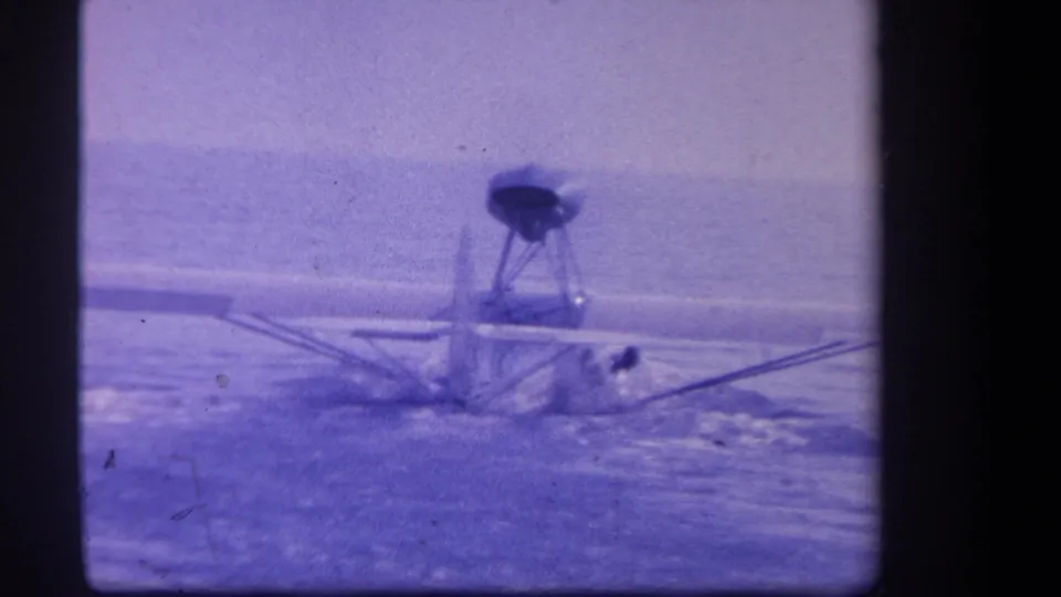 A 1959 Yucaipa home-movie frame shows the small float plane continuing across the lake, with its tail and pontoons visible through soft focus.