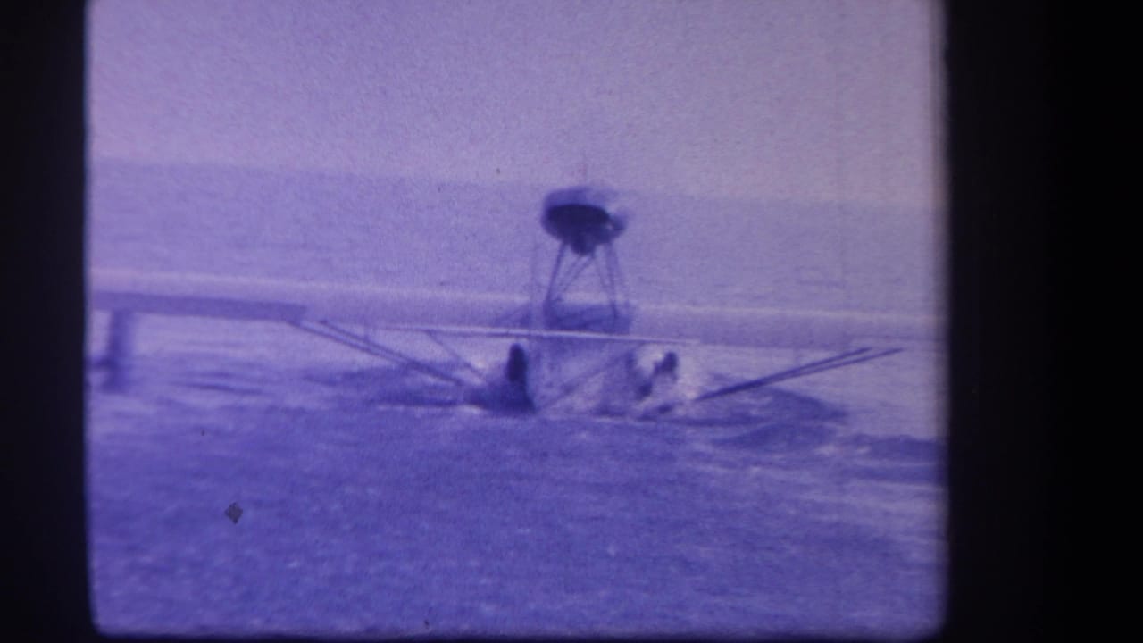 Seaplane sits low on calm water with wing and float structure visible in soft focus.