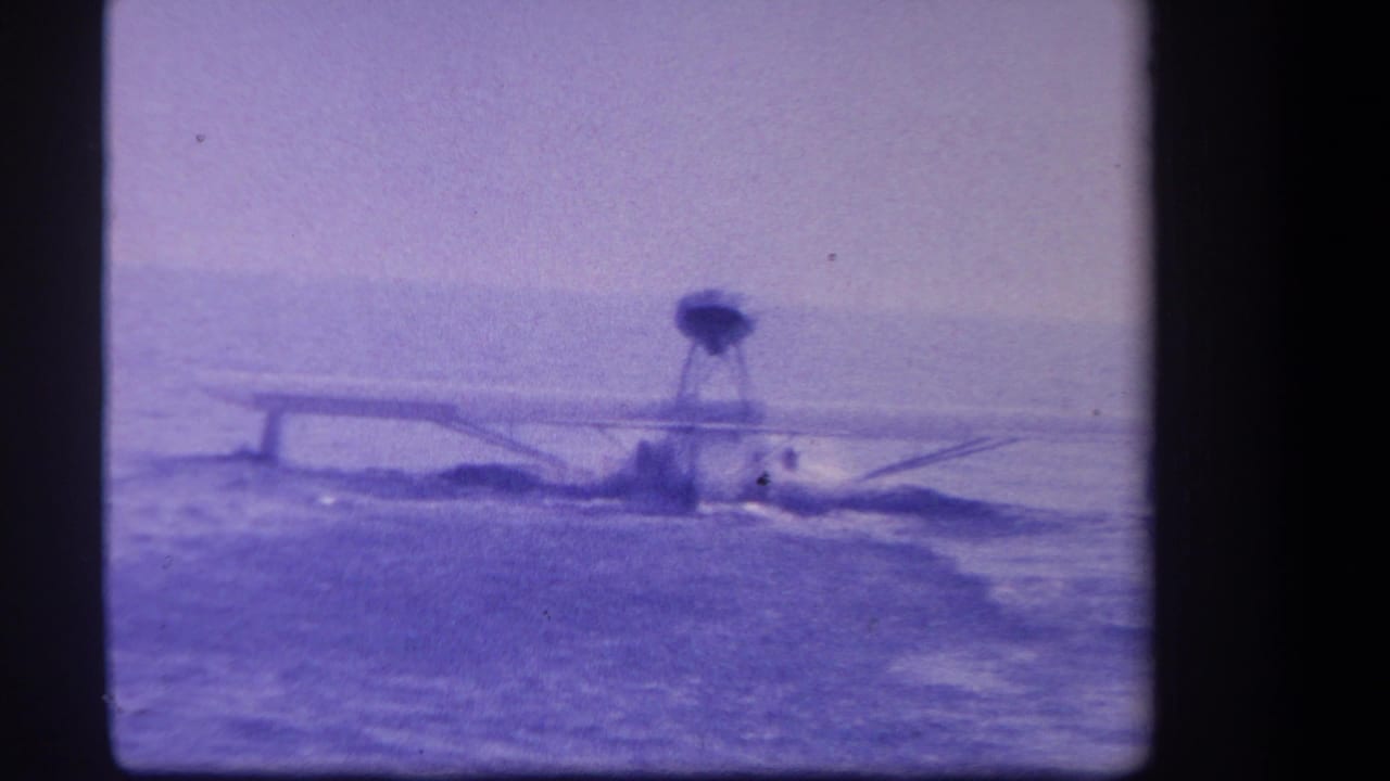 Small seaplane moving across lake water with wake and dark film borders.