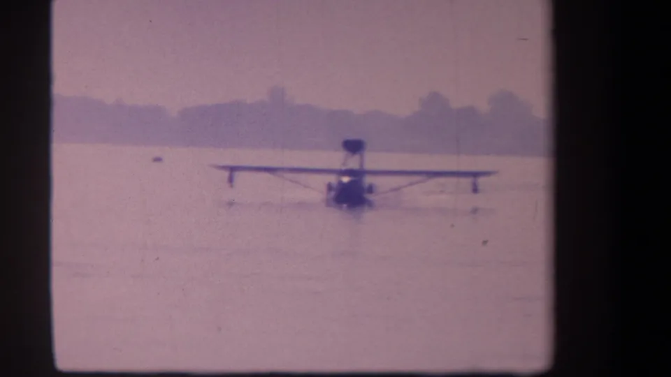 Final 1959 Volmer Yucaipa frame with the floatplane moving across calm water beneath a softly faded sky.