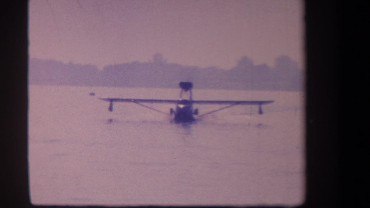 1959 8mm frame of a distant seaplane or flying boat approaching across calm water near Volmer Yucaipa, California.