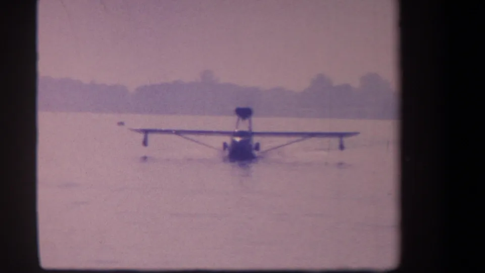 1959 8mm frame of a distant seaplane or flying boat approaching across calm water near Volmer Yucaipa, California.
