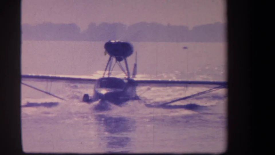 1959 8mm frame showing the aircraft nearly head-on, skimming or settling on the water with wake trailing behind.