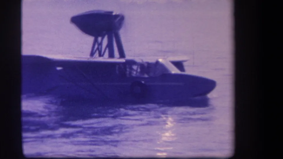 Close 1959 8mm side view of the seaplane or flying boat moving on water, with cockpit and upper structure silhouetted.