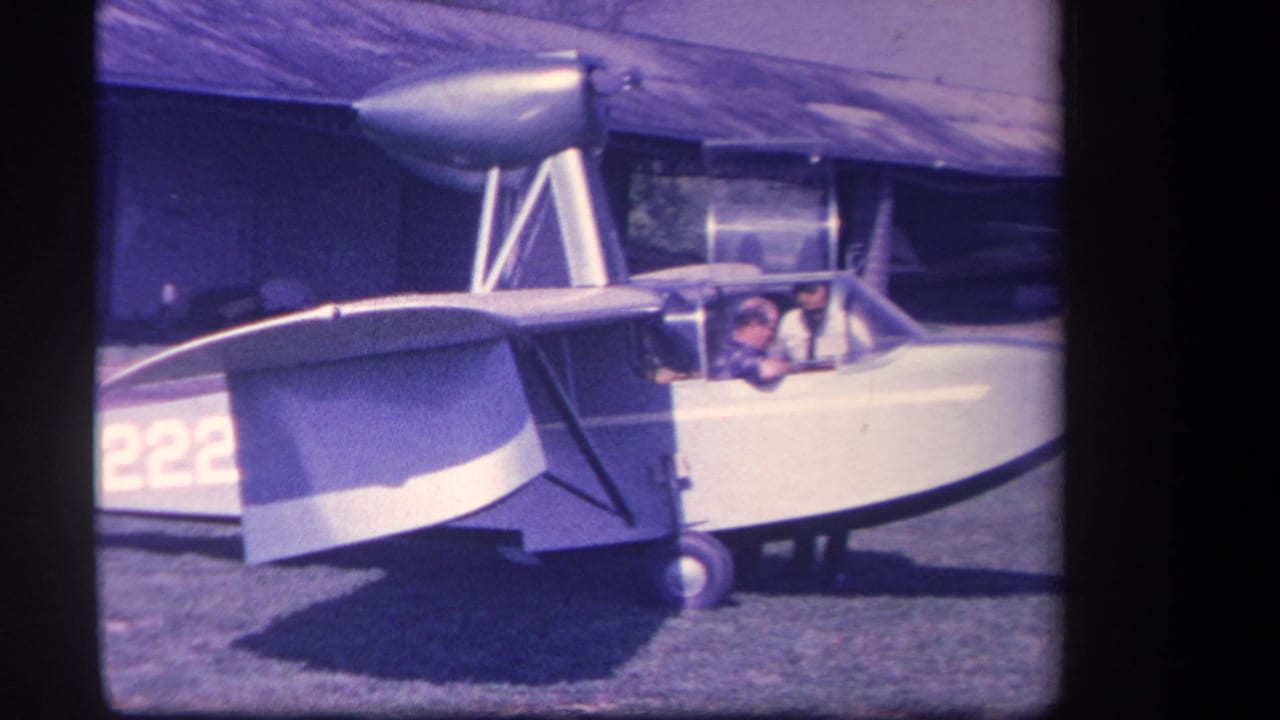 Amphibious aircraft side view with men in the cockpit and partial tail number visible.