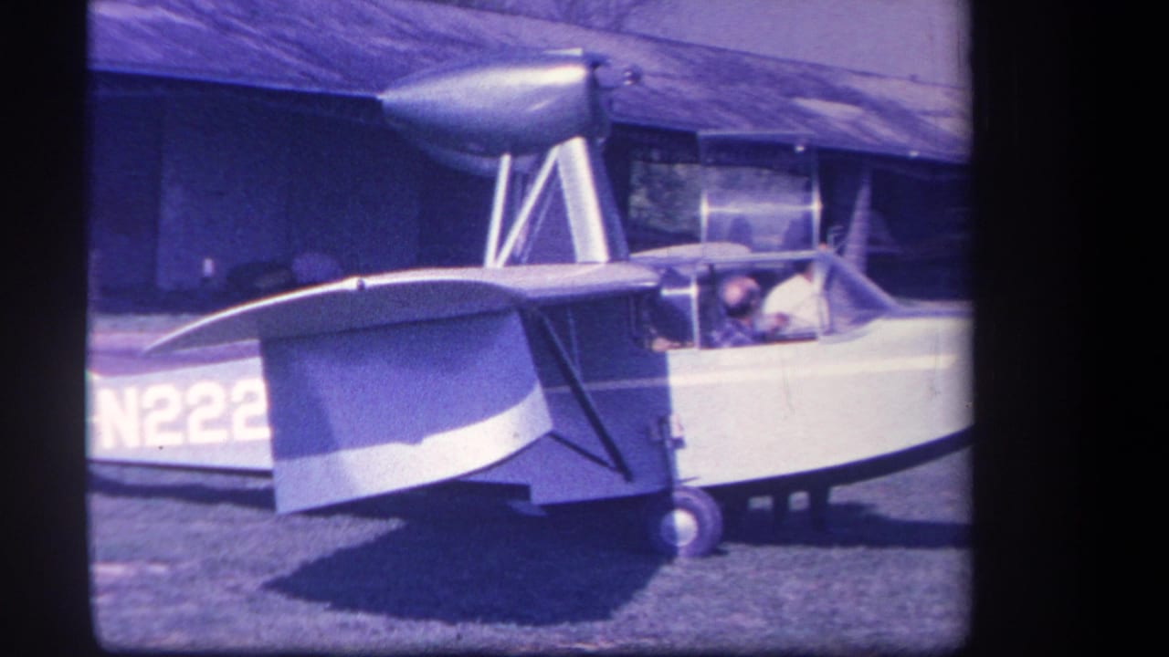 1959 Yucaipa home-movie frame showing a small amphibious aircraft on grass with two occupants visible through the cockpit.