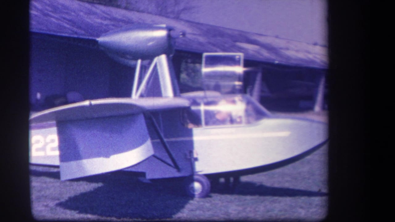 Partial side view of a small light aircraft parked on grass near a building.