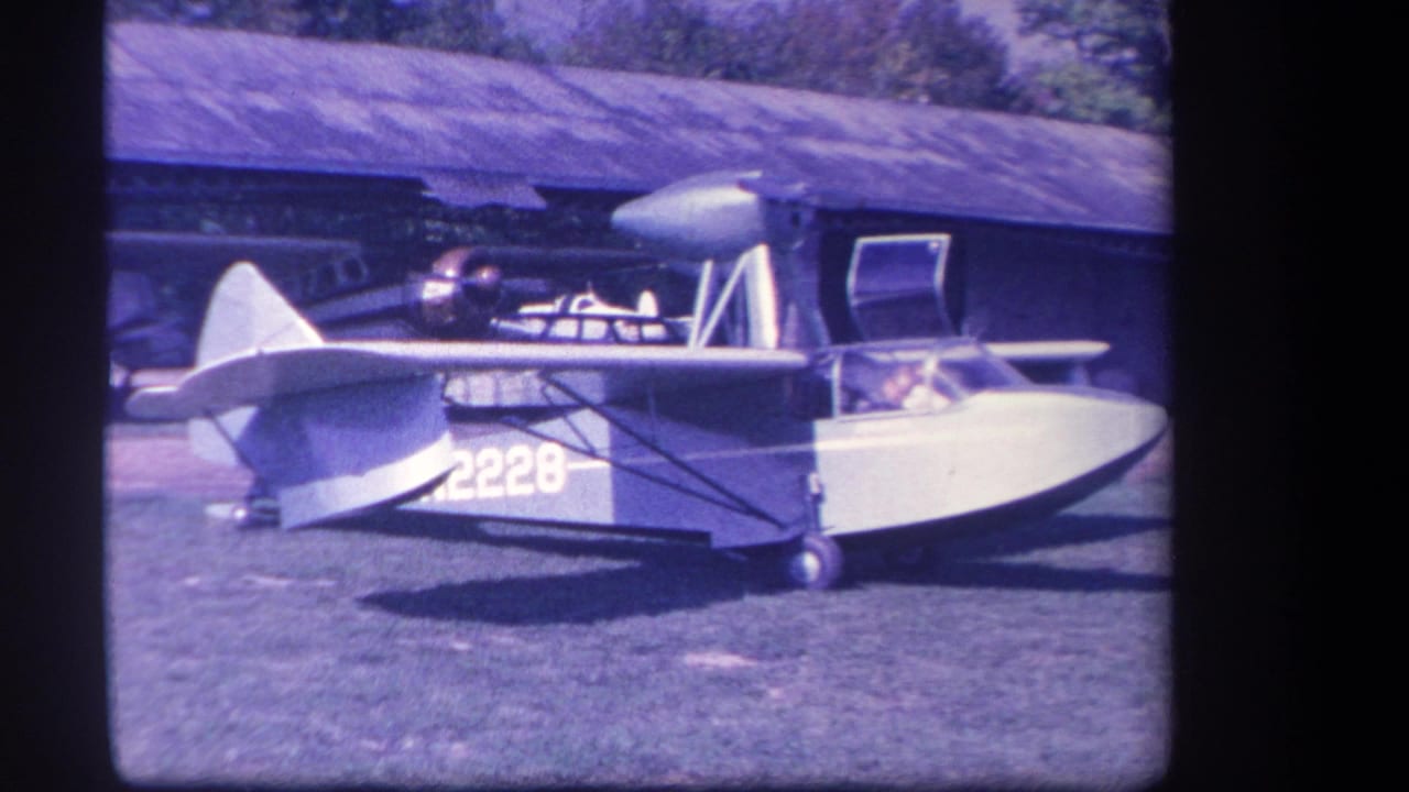 Small amphibious aircraft parked on grass beside a barn-like building.