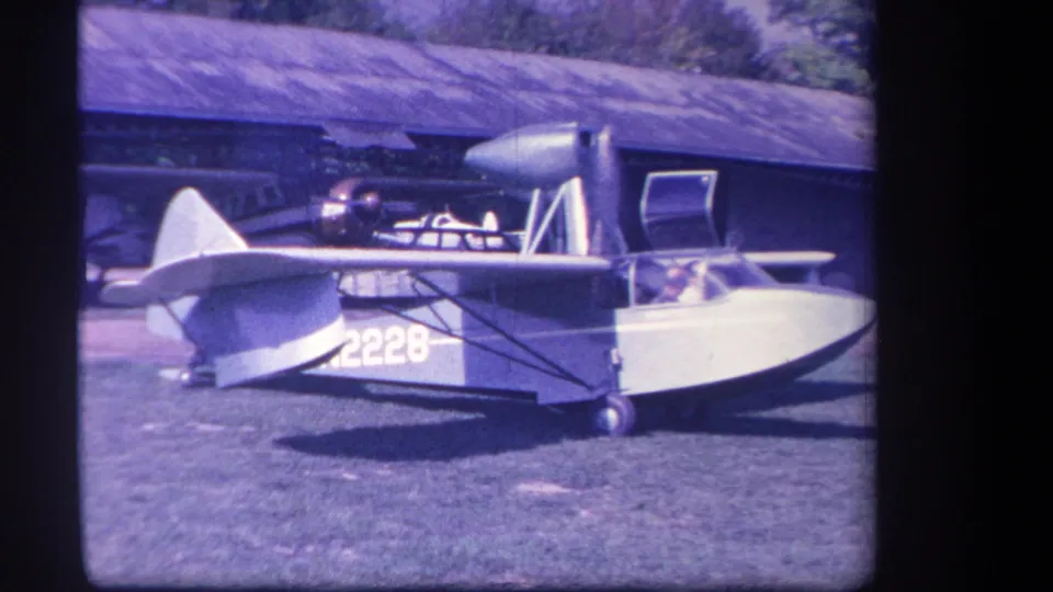 Yucaipa, California home-movie frame showing a small amphibious aircraft on grass, with N2228 markings and a person in the cockpit.