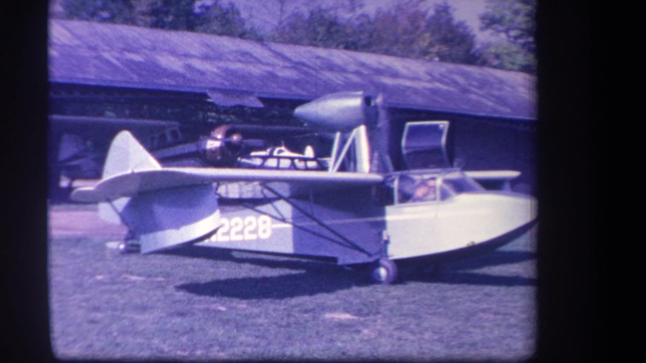 1959 Yucaipa footage shows an amphibious airplane marked 2228 on a grass field near a hangar, with its propeller running and a cockpit occupant visible.