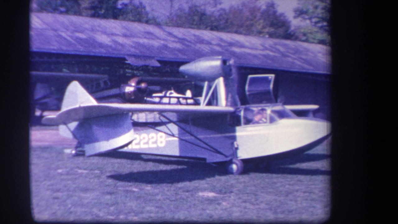 The amphibious aircraft remains parked on the grass in Yucaipa, with number 2228 visible, the cockpit door open, and a person seated inside.