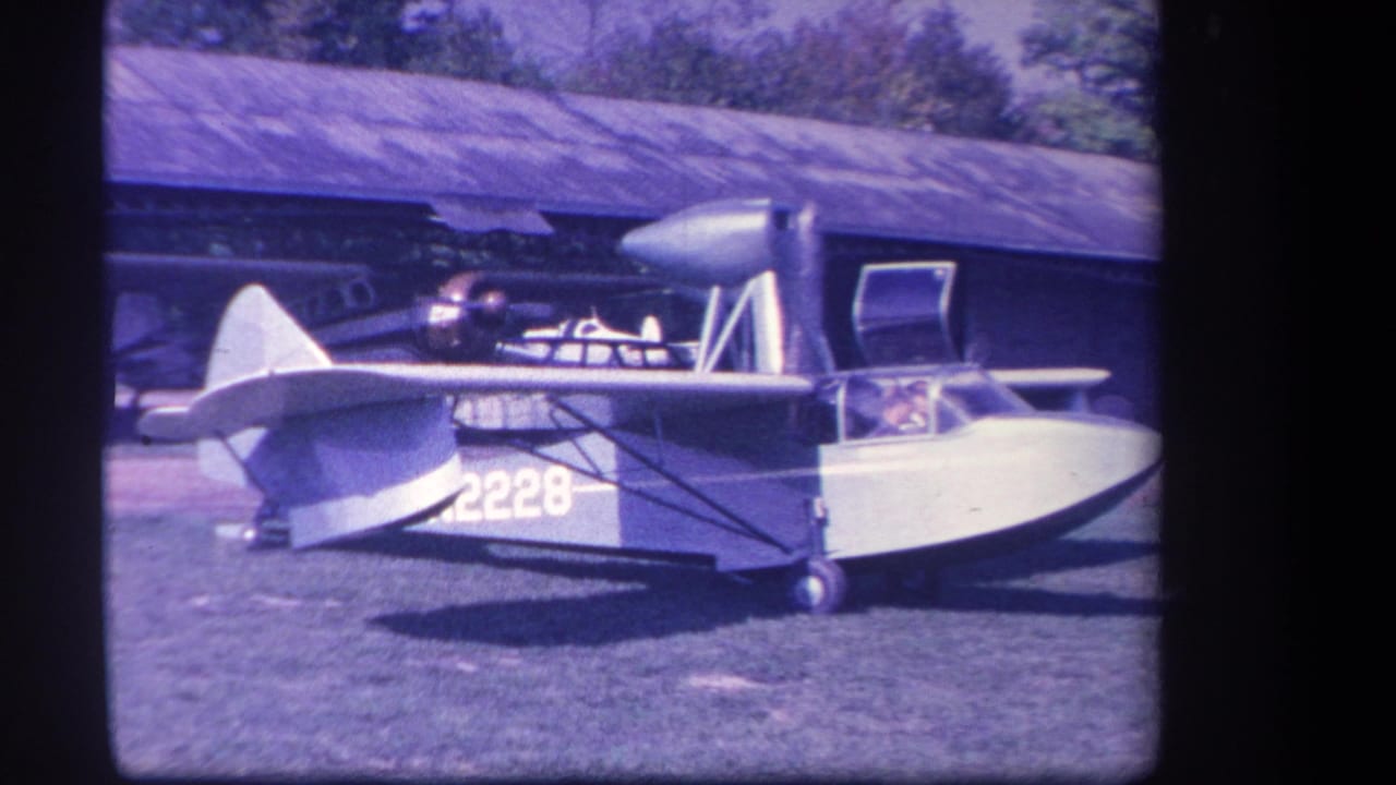 1959 Yucaipa-area home-movie frame showing a small blue and white amphibious aircraft with number 2228 beside a hangar.