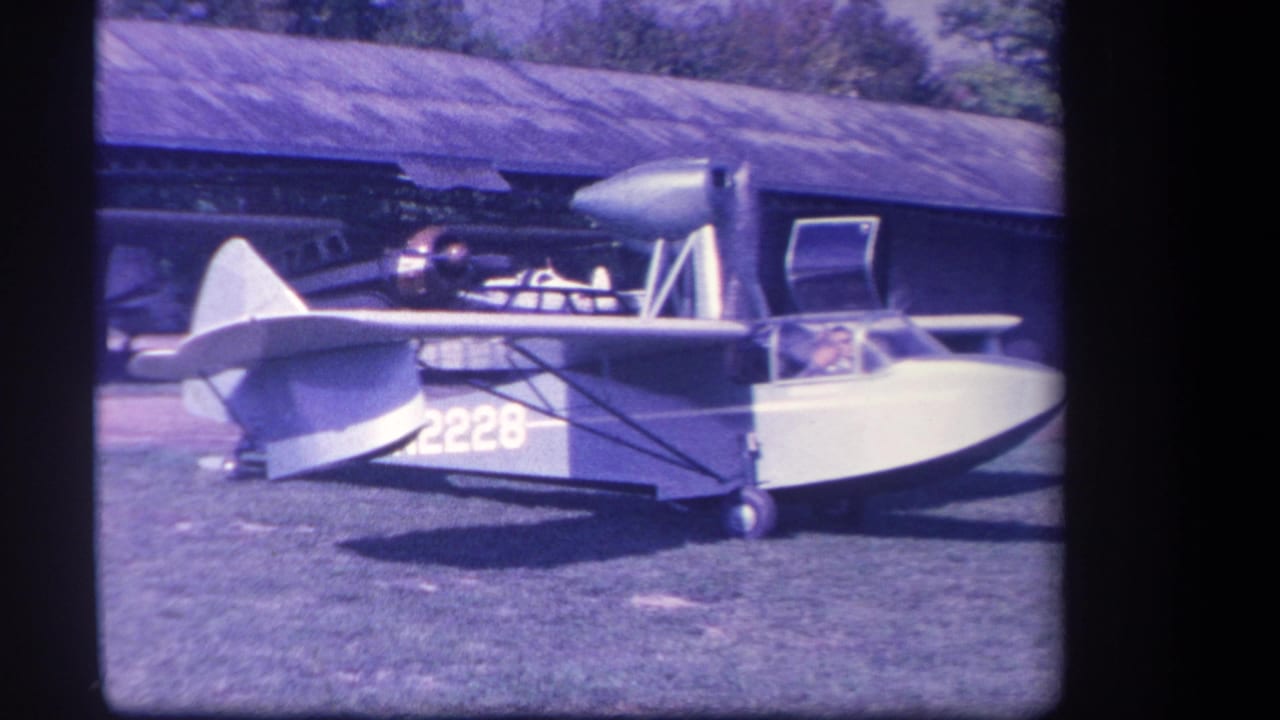 Side view of the amphibious aircraft with cockpit, propeller, and hangar behind it.