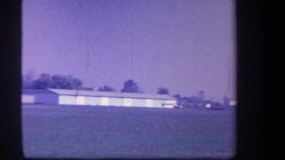 Distant view of a rural Yucaipa-area airfield in 1959, with a low hangar and small plane near the tree line.