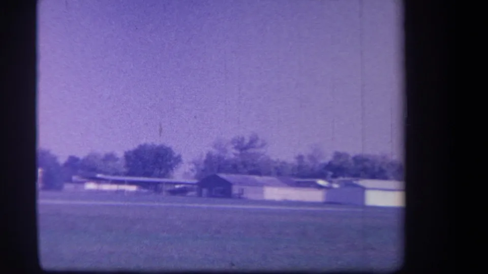 Yucaipa-area 1959 home-movie frame showing airfield buildings, a small aircraft, trees, and aged purple color shift.
