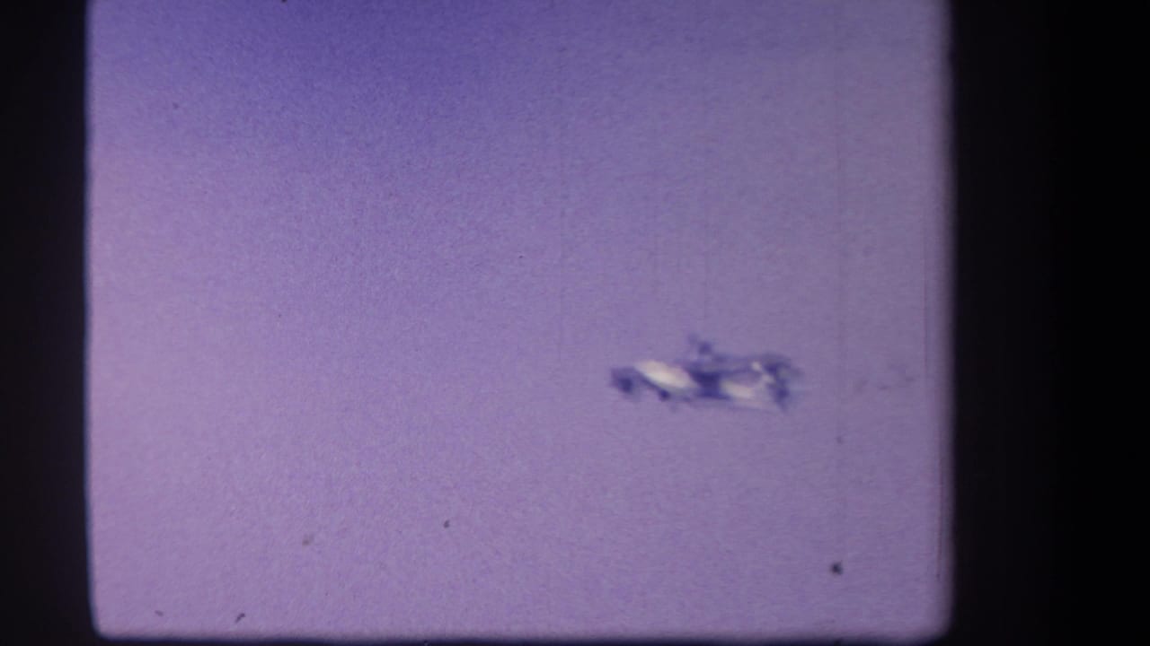 A small white twin-motor airplane appears distant against a purple-tinted sky in 1959 home-movie footage from Yucaipa, California.