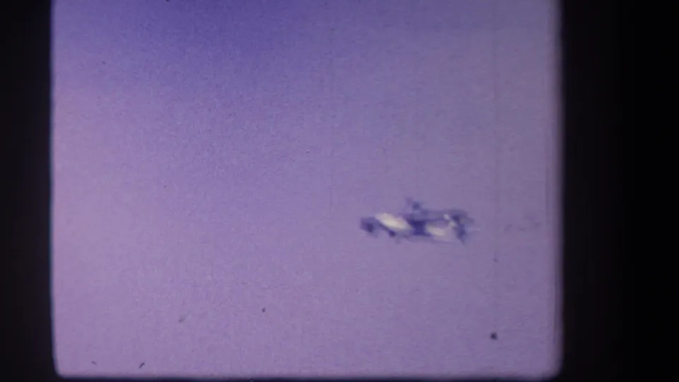A small white twin-motor airplane appears distant against a purple-tinted sky in 1959 home-movie footage from Yucaipa, California.