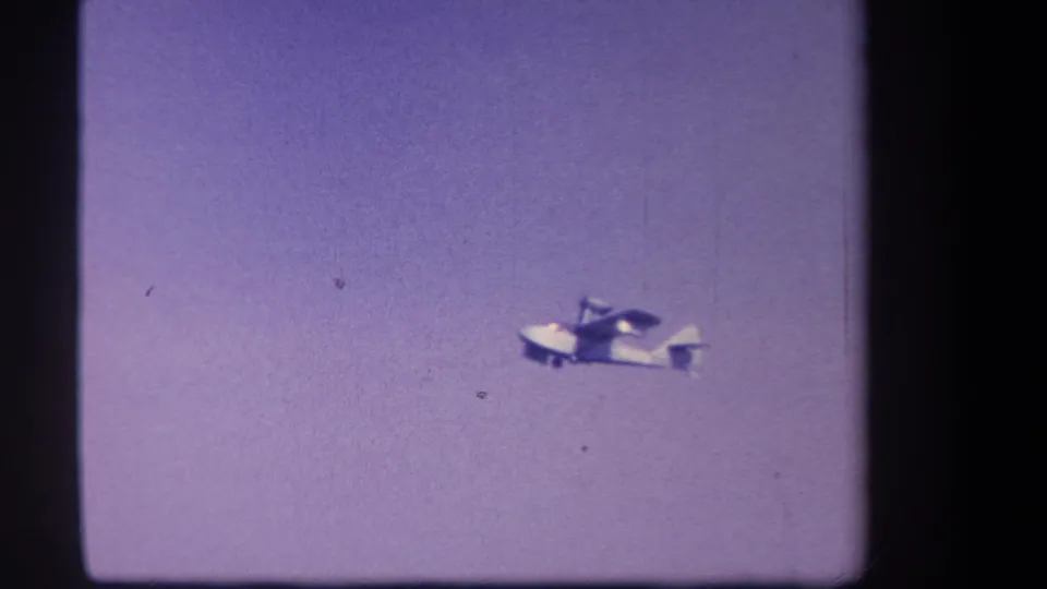 The white twin-motor airplane is seen more clearly against the purple sky, with 8mm frame edges and visible film texture.