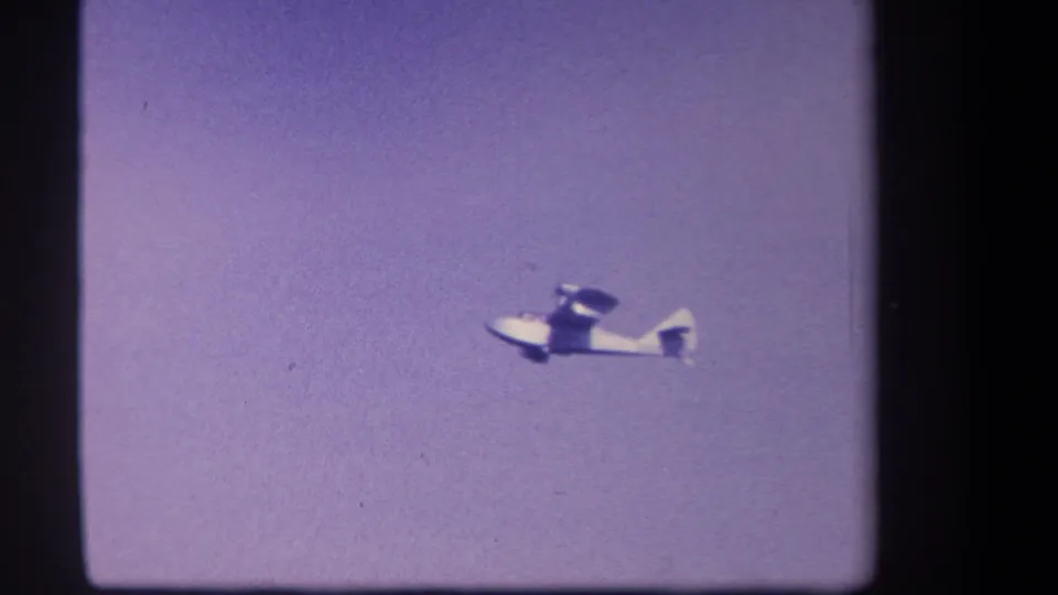 A white twin-motor aircraft crosses the lower part of the frame in grainy 8mm footage from the 1959 Yucaipa clip.