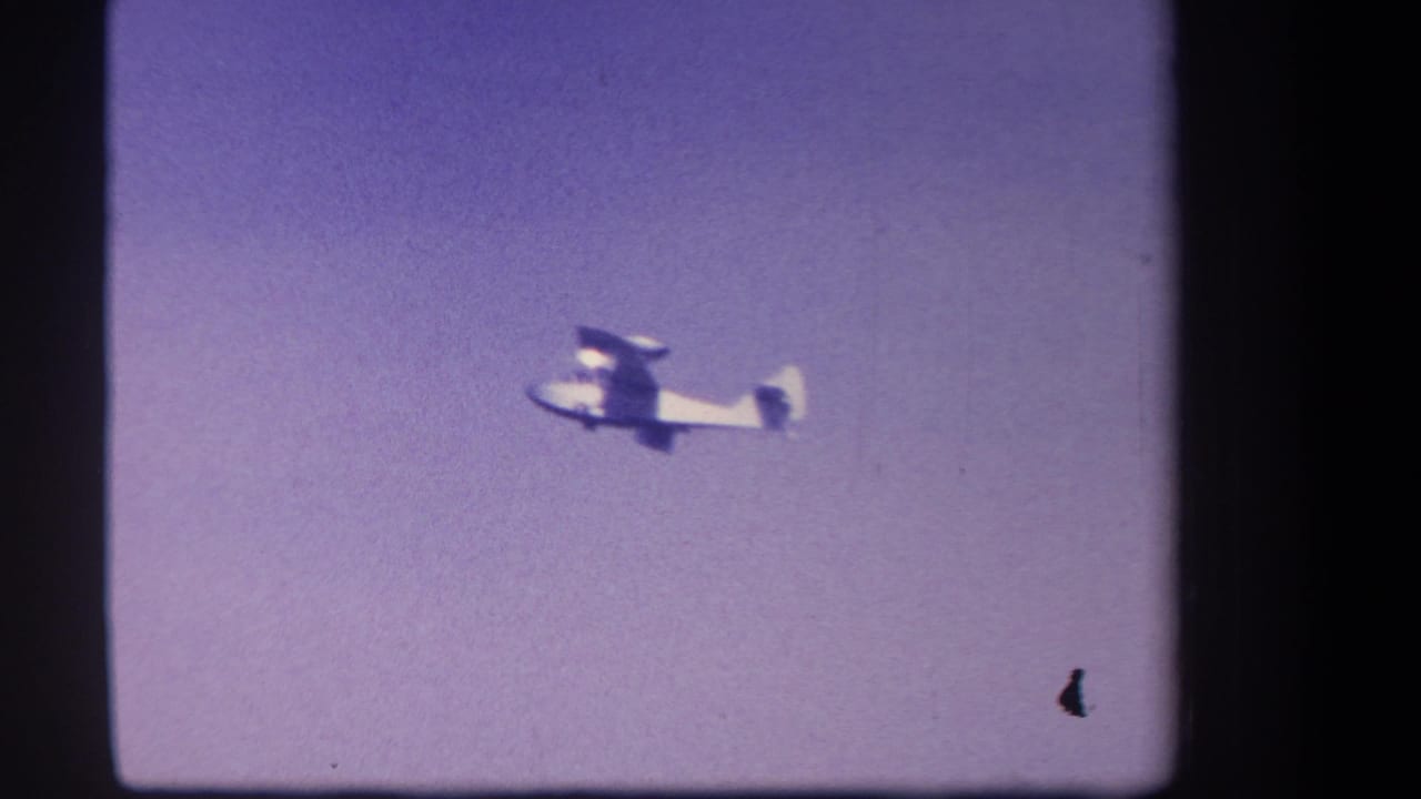 Small propeller plane seen in distant flight against a purple-tinted sky in 1959 Yucaipa, California 8mm footage.