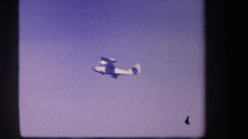 Small propeller plane seen in distant flight against a purple-tinted sky in 1959 Yucaipa, California 8mm footage.