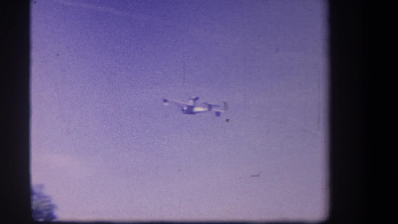 A small aircraft appears in flight against a purple-tinted sky in 1959 home-movie footage from Yucaipa, California.