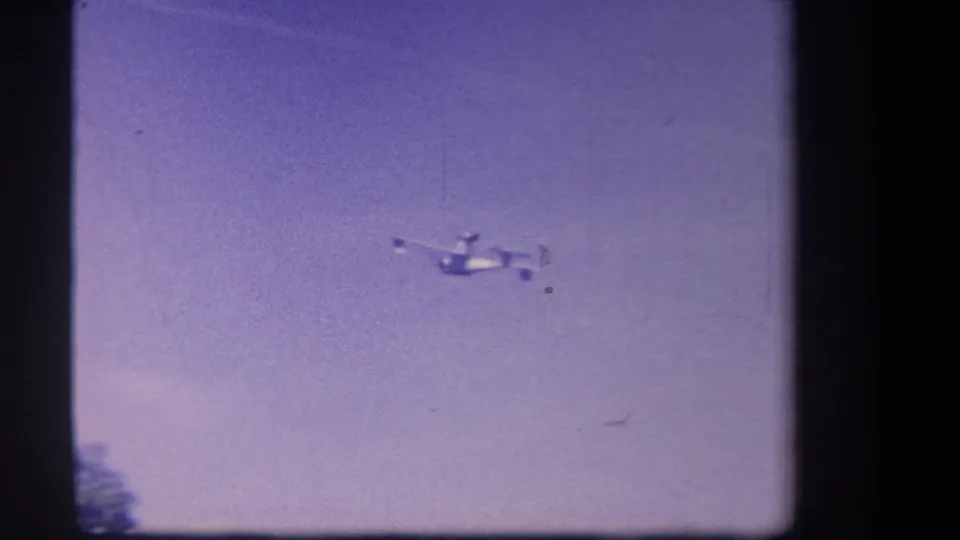 A small aircraft appears in flight against a purple-tinted sky in 1959 home-movie footage from Yucaipa, California.