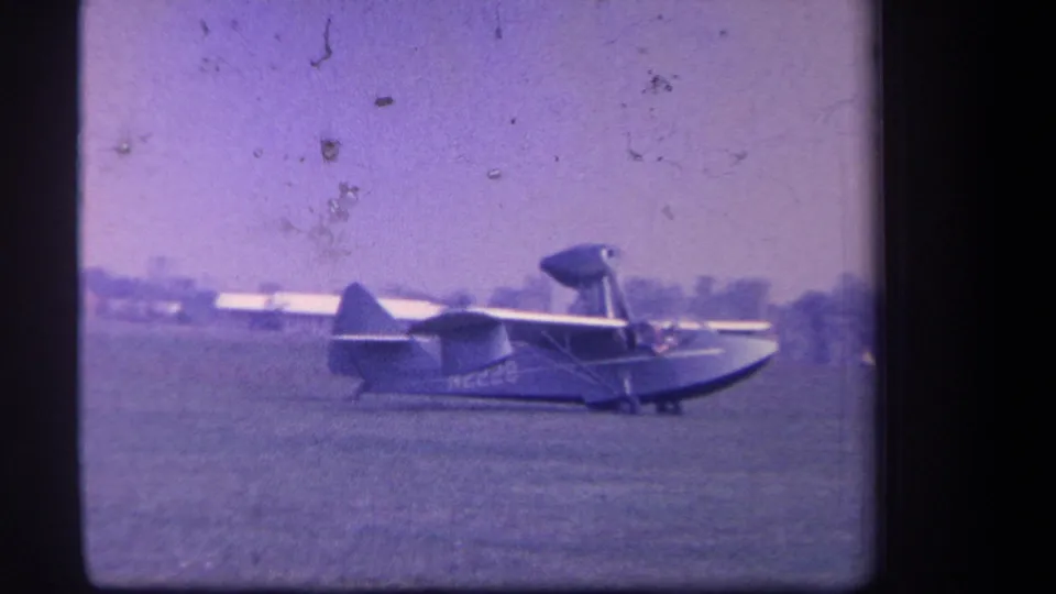 1959 Yucaipa, California home-movie frame showing a Volmer amphibian aircraft moving across a grass airfield under a pale sky.