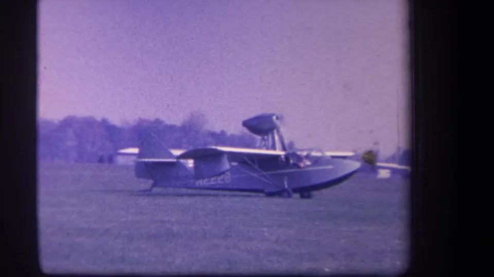 A closer 1959 home-movie frame shows the amphibian aircraft taxiing on grass, with fuselage markings and the cockpit area visible.