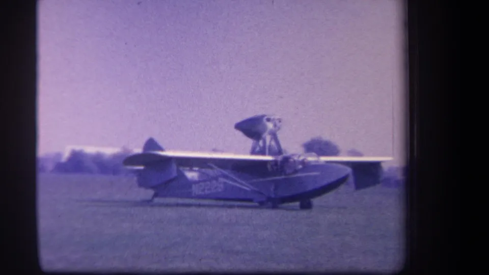 Side view of the amphibious aircraft on the Yucaipa grass field, with its high wing and registration marking visible in soft 8mm color.