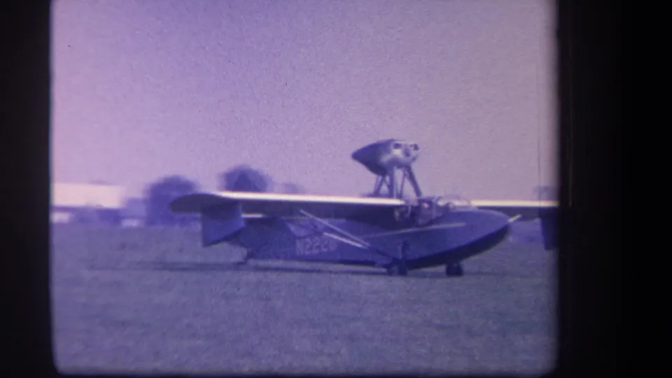 Closer 1959 home-movie frame of the amphibious aircraft taxiing, with the wing, hull-like fuselage, and tail surfaces prominent.