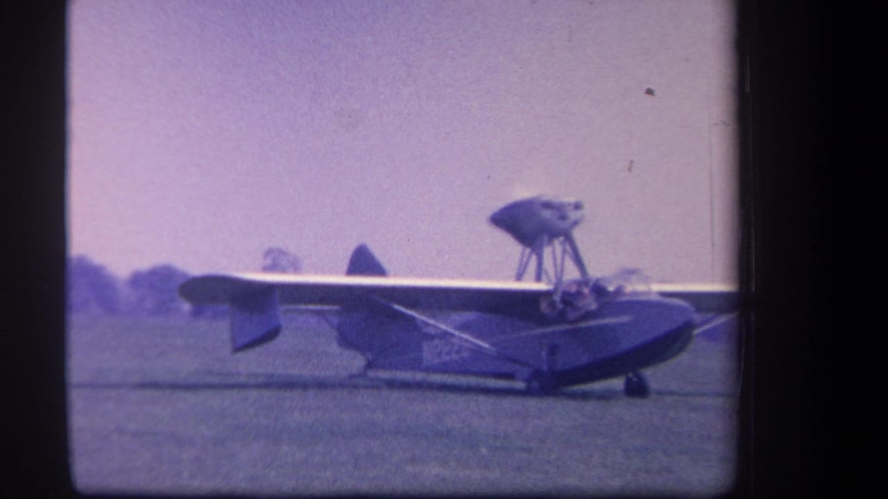 1959 Yucaipa home-movie frame showing a small propeller aircraft on a grassy airfield with soft purple 8mm color shift.