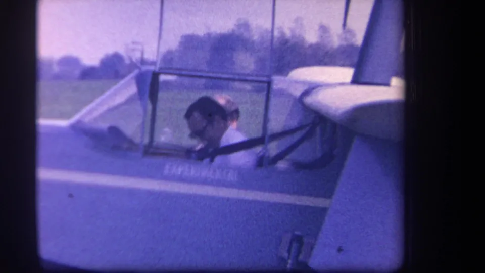 A pilot sits inside the cockpit of the small experimental aircraft, filmed in soft purple-tinted 8mm footage in Yucaipa.