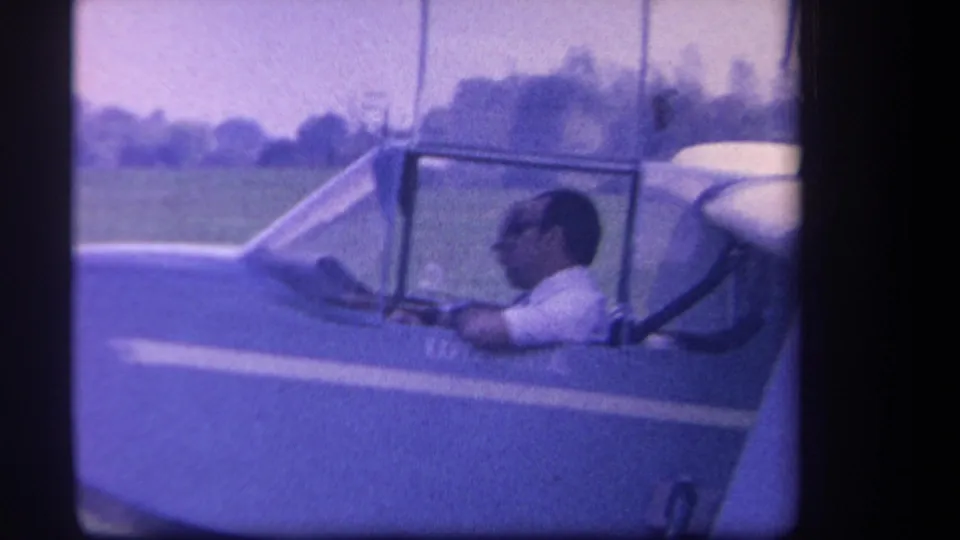 1959 Yucaipa side view of the pilot seated in the experimental glider cockpit with open field and trees behind him.
