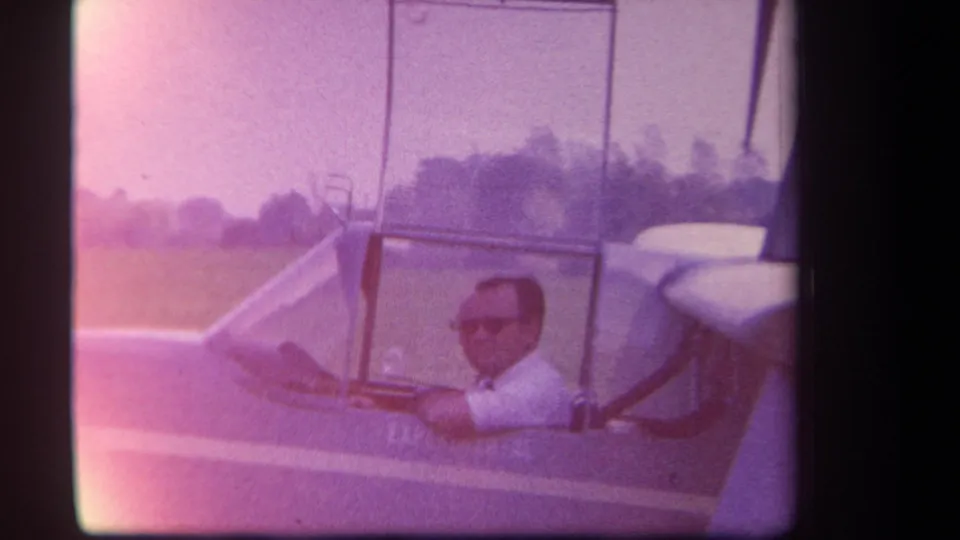 1959 Yucaipa-area 8mm frame with pink color cast showing a pilot in sunglasses inside a small experimental aircraft.