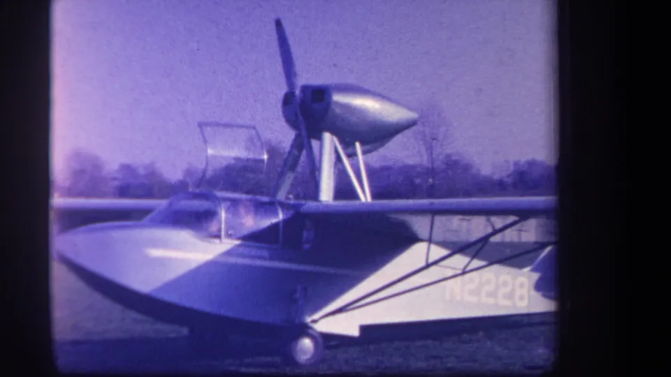 1959 home-movie frame from Yucaipa, California, showing aircraft N2228 with a high wing, canopy, and propeller assembly on grass.